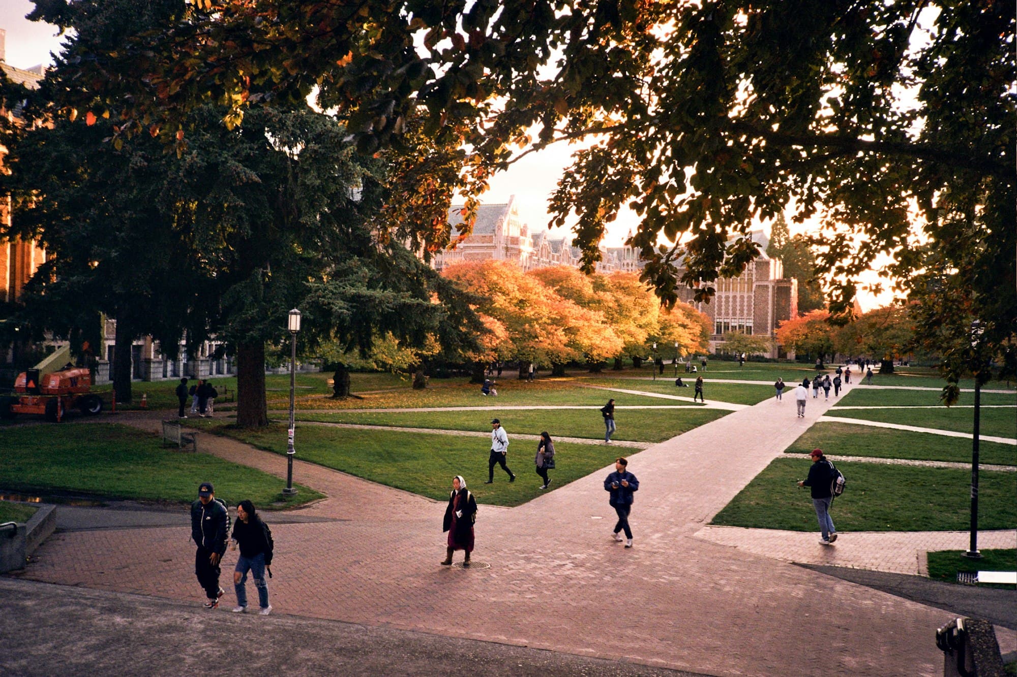 Students walking across a tree-lined university quad at golden hour, with autumn foliage in front of historic college buildings